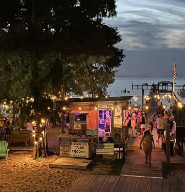 American Legion waterfront grounds in Fairhope, Alabama, with a tiki bar, beach seating, and Mobile Bay views.